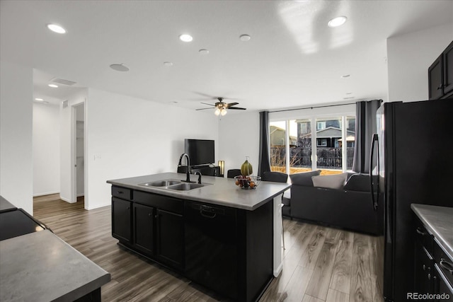 kitchen with sink, ceiling fan, black appliances, an island with sink, and dark hardwood / wood-style flooring