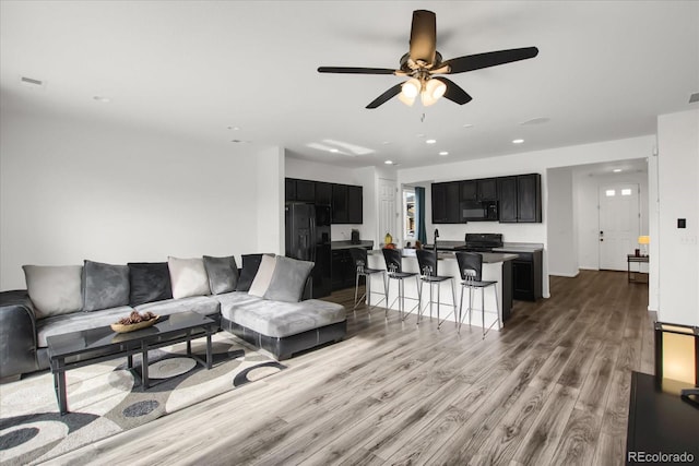 living room featuring ceiling fan, sink, and light wood-type flooring