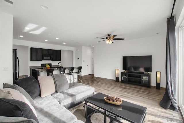 living room featuring sink, ceiling fan, and light wood-type flooring