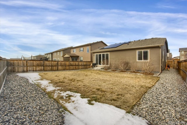 rear view of house with solar panels and a fenced backyard