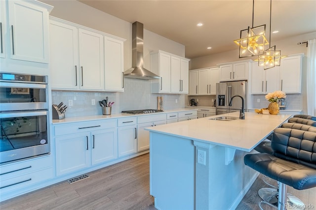 kitchen featuring sink, wall chimney range hood, pendant lighting, white cabinets, and appliances with stainless steel finishes