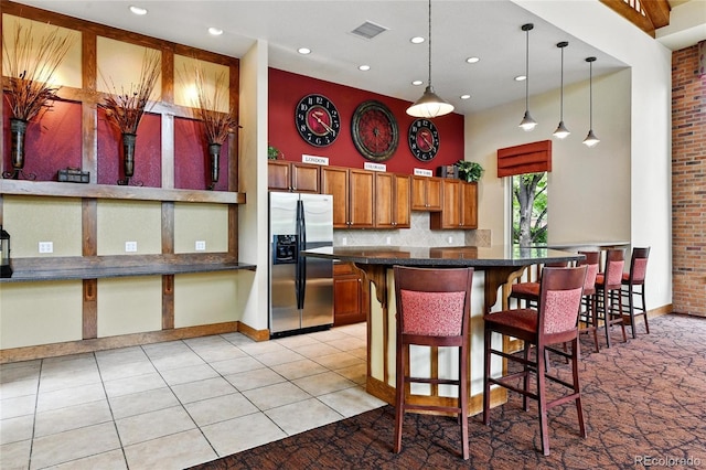 7931 W 55th Ave Unit 105, Arvada, CO 80002 - kitchen with stainless steel fridge, dark countertops, a towering ceiling, a breakfast bar area, and brown cabinetry