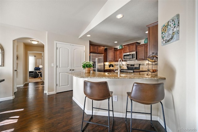 kitchen with kitchen peninsula, appliances with stainless steel finishes, backsplash, light stone counters, and sink