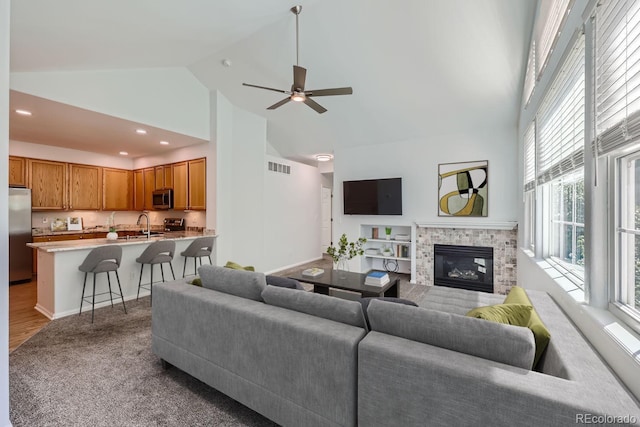 living room featuring a fireplace, high vaulted ceiling, light hardwood / wood-style flooring, sink, and ceiling fan