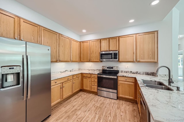 kitchen with appliances with stainless steel finishes, light stone countertops, light hardwood / wood-style floors, and sink