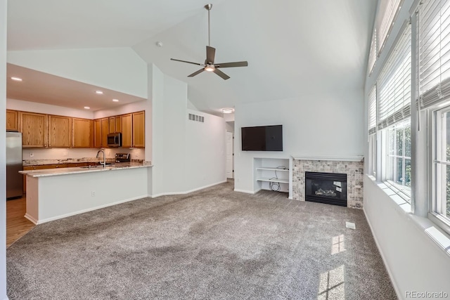 unfurnished living room with a stone fireplace, light carpet, sink, high vaulted ceiling, and ceiling fan