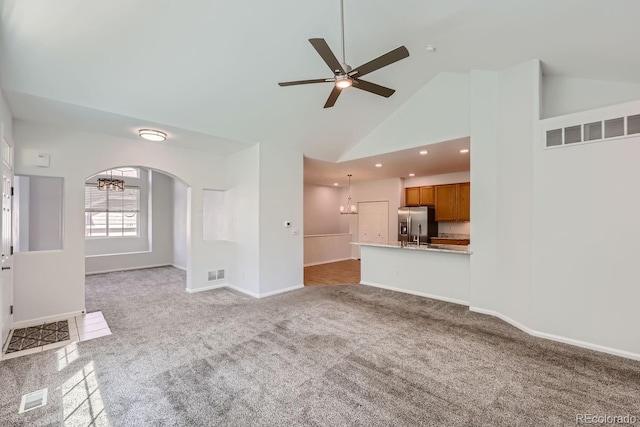 unfurnished living room with light colored carpet, ceiling fan with notable chandelier, and high vaulted ceiling