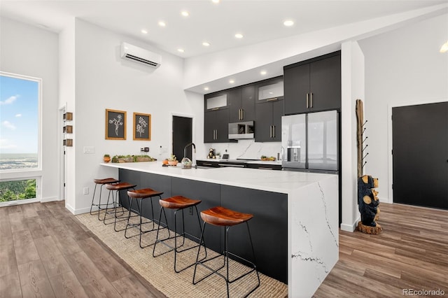 555 Sunrise Peak Rd, Manitou Springs, CO 80829 - kitchen with white microwave, dark cabinetry, a breakfast bar, a peninsula, and a wall mounted air conditioner
