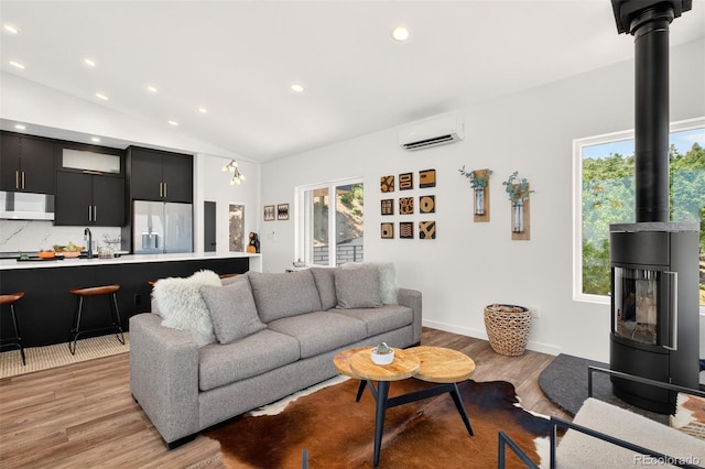 555 Sunrise Peak Rd, Manitou Springs, CO 80829 - living area featuring a wall unit AC, a wood stove, plenty of natural light, light wood-style flooring, and vaulted ceiling