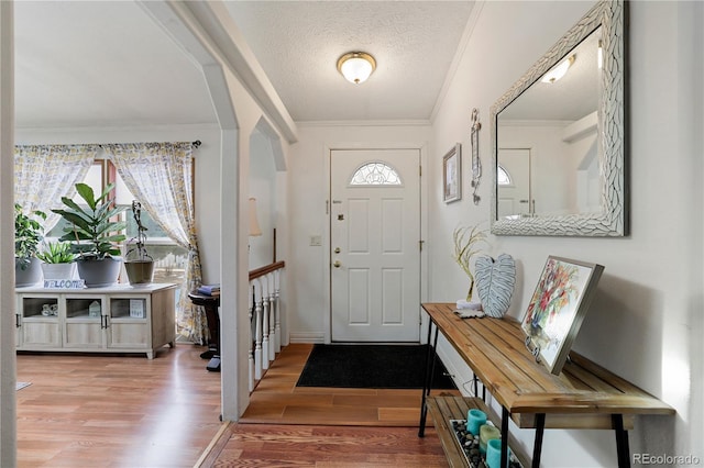 entryway with a textured ceiling, crown molding, and wood-type flooring