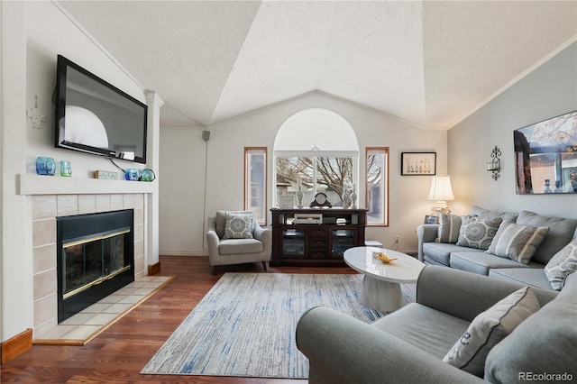 living room featuring a tiled fireplace, vaulted ceiling, a textured ceiling, and wood-type flooring