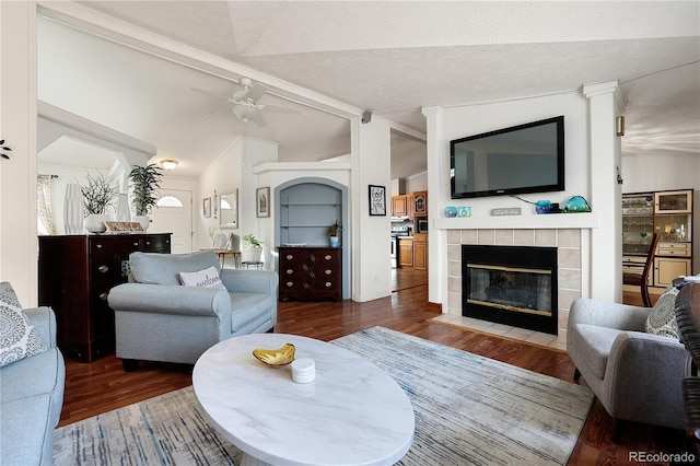 living room with a tiled fireplace, ceiling fan, lofted ceiling with beams, and dark hardwood / wood-style flooring