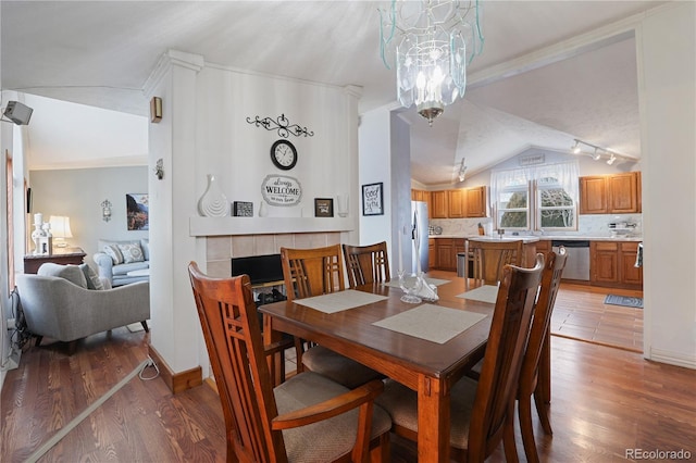 dining area with lofted ceiling, a tile fireplace, hardwood / wood-style flooring, and a chandelier