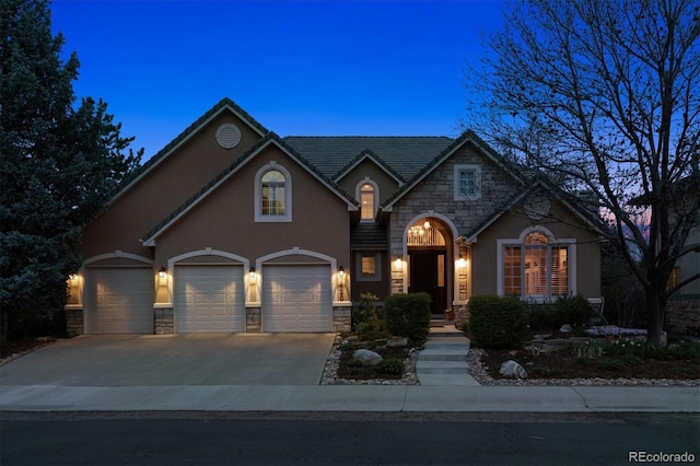 view of front facade with a garage, stucco siding, stone siding, and concrete driveway