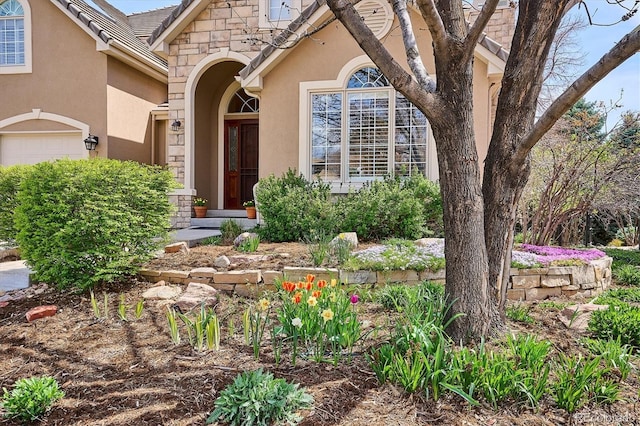 view of exterior entry featuring a garage, stucco siding, and stone siding