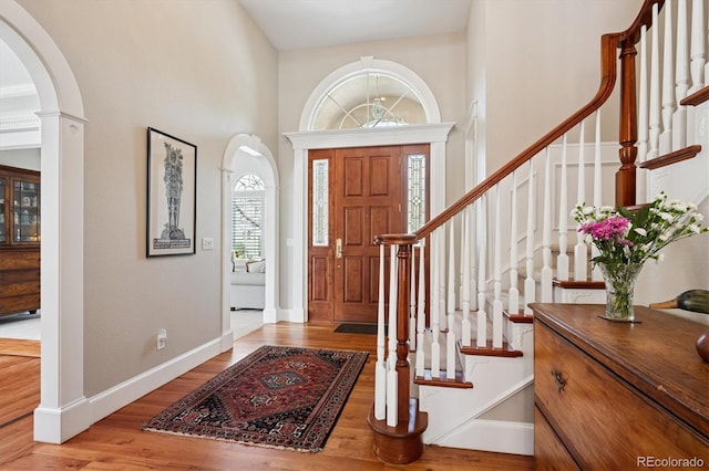 entrance foyer featuring stairs, a towering ceiling, wood finished floors, baseboards, and arched walkways