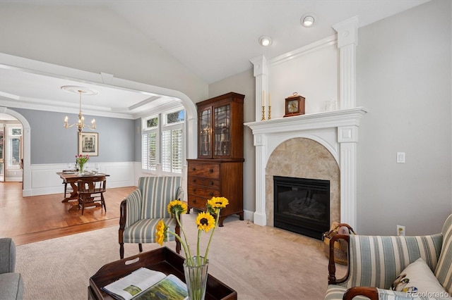 living room with light colored carpet, arched walkways, a glass covered fireplace, a wainscoted wall, and light wood-type flooring