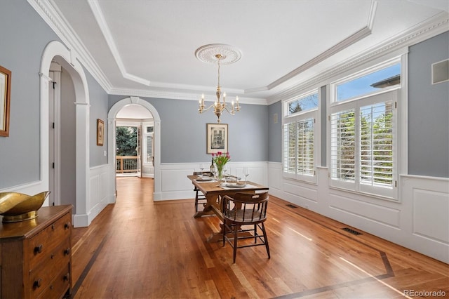 dining area with a notable chandelier, arched walkways, light wood-type flooring, a tray ceiling, and visible vents