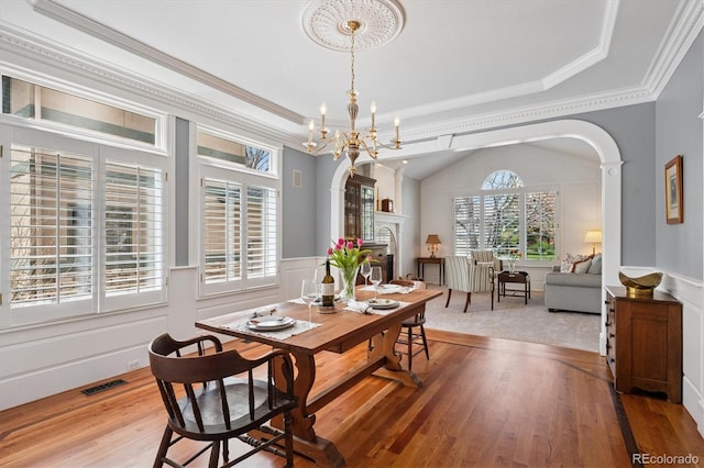 dining area with an inviting chandelier, arched walkways, a wainscoted wall, wood finished floors, and visible vents