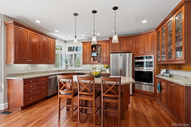 kitchen featuring glass insert cabinets, light wood-style floors, a center island, a sink, and stainless steel appliances