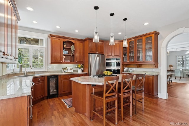 kitchen with appliances with stainless steel finishes, a sink, beverage cooler, arched walkways, and brown cabinetry