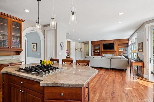 kitchen featuring stainless steel gas cooktop, a breakfast bar, recessed lighting, arched walkways, and light wood-style flooring