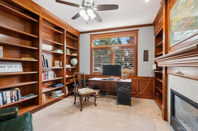 office space featuring crown molding, wainscoting, light carpet, a tiled fireplace, and a ceiling fan