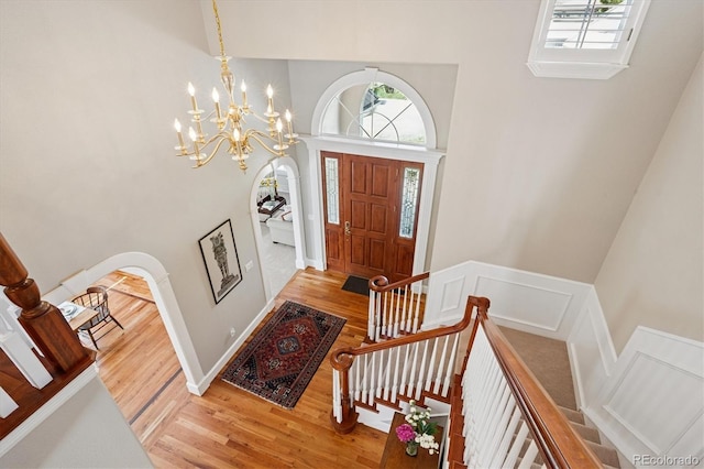 foyer with arched walkways, light wood finished floors, a towering ceiling, and a chandelier