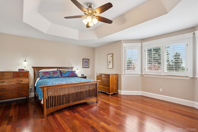 bedroom with a ceiling fan, baseboards, a raised ceiling, and hardwood / wood-style floors