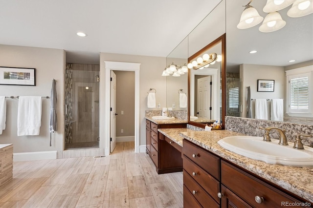 bathroom with wood finished floors, baseboards, two vanities, a shower stall, and a sink