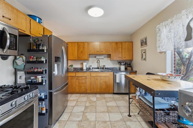 kitchen with dark countertops, brown cabinetry, a sink, and stainless steel appliances