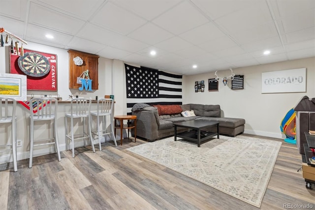 living area featuring a drop ceiling, recessed lighting, baseboards, and wood finished floors