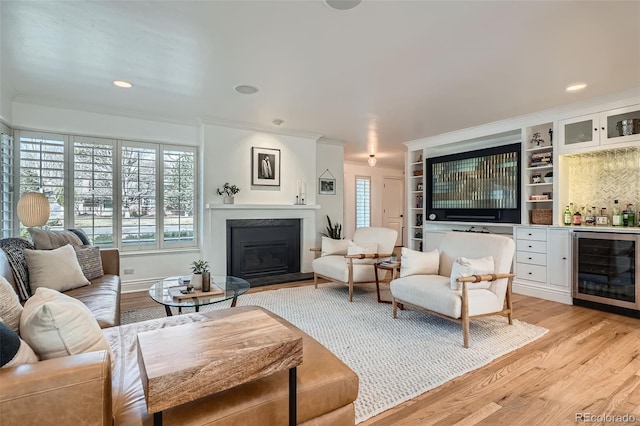 living area featuring light wood-style flooring, ornamental molding, wine cooler, a glass covered fireplace, and indoor bar