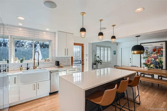 kitchen with white cabinetry, light wood-style flooring, a sink, light countertops, and dishwasher