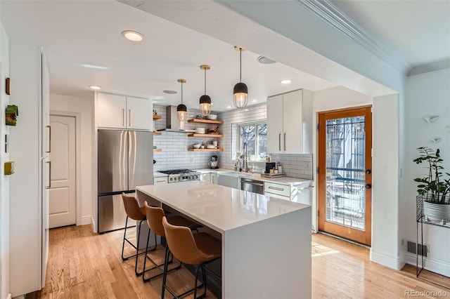 kitchen featuring a kitchen bar, open shelves, appliances with stainless steel finishes, light wood finished floors, and light countertops