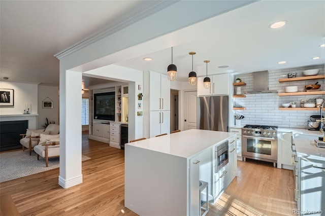 kitchen with wall chimney range hood, light wood-style floors, white cabinets, stainless steel appliances, and open shelves