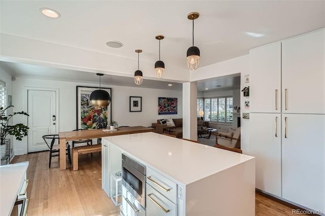 kitchen with light countertops, white cabinets, stainless steel microwave, light wood-type flooring, and a center island