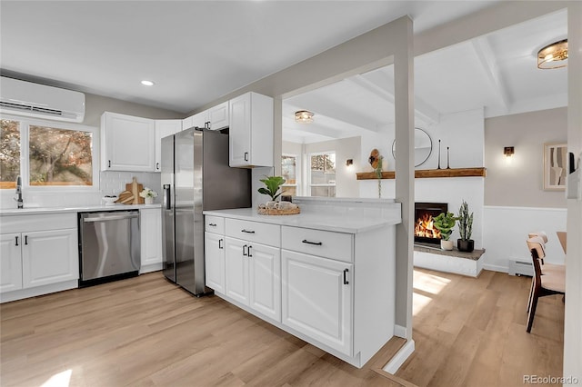 kitchen with an AC wall unit, plenty of natural light, white cabinetry, and appliances with stainless steel finishes