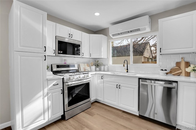 kitchen with an AC wall unit, appliances with stainless steel finishes, sink, and white cabinetry