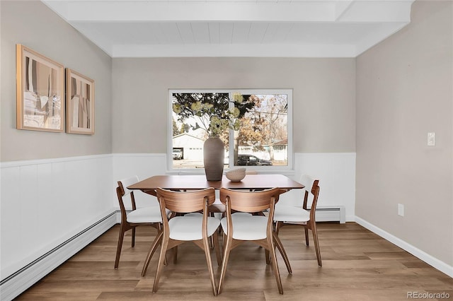 dining space featuring a baseboard radiator, beamed ceiling, and light wood-type flooring