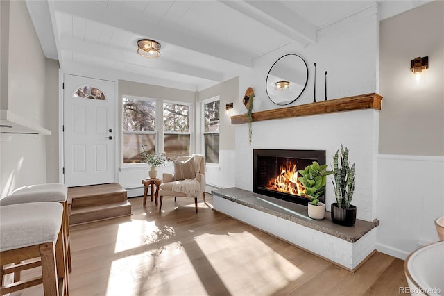 living area with light hardwood / wood-style floors, baseboard heating, and beamed ceiling