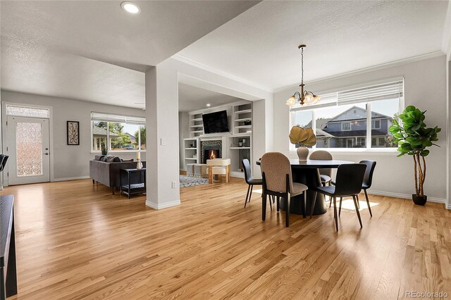 3406 Purcell St, Brighton, CO 80601 - dining space featuring a lit fireplace, light wood-type flooring, crown molding, baseboards, and a chandelier