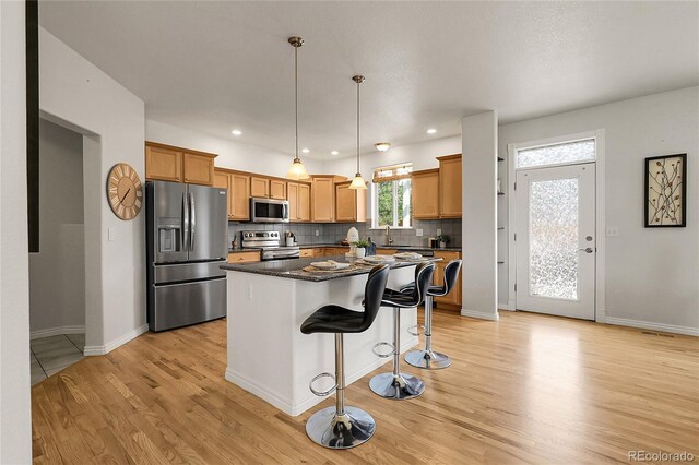 3406 Purcell St, Brighton, CO 80601 - kitchen featuring stainless steel appliances, dark countertops, light wood finished floors, a kitchen breakfast bar, and decorative backsplash