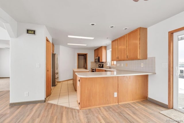 kitchen with sink, light hardwood / wood-style flooring, appliances with stainless steel finishes, decorative backsplash, and kitchen peninsula