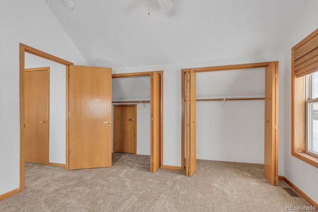 unfurnished bedroom with lofted ceiling, two closets, light carpet, and ceiling fan