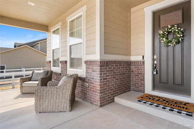 entrance to property with brick siding, covered porch, and fence
