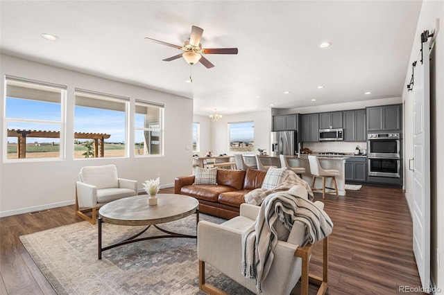 living room featuring plenty of natural light, baseboards, a barn door, and ceiling fan with notable chandelier