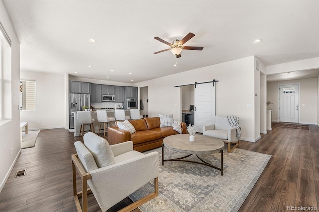 living area with baseboards, dark wood-type flooring, a barn door, and a ceiling fan