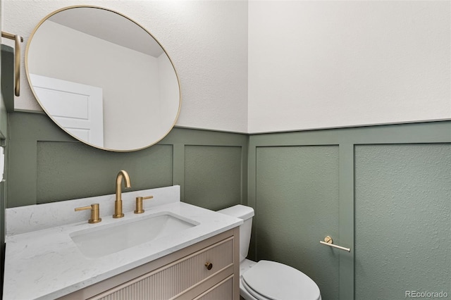 bathroom featuring vanity, toilet, and a decorative wall