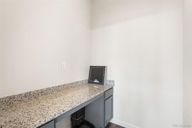 unfurnished office with built in study area, baseboards, and dark wood-style floors
